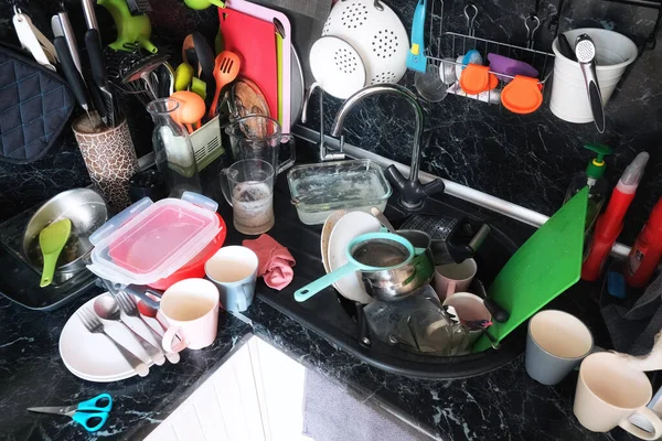 The mess in the modern kitchen. No washed dishes, pots and pans in the kitchen sink. A lot of dirty dishes after Breakfast, lunch and dinner on the table top.