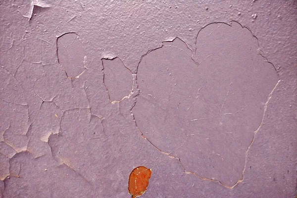Peeling paint on metal in the shape of a heart, a dirty red surface background