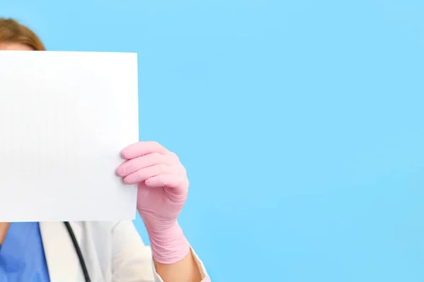 Woman nurse with a sheet of paper on a blue background, copy space