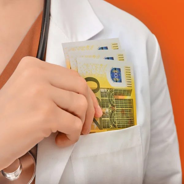 Doctor in medical clothes with euro money, orange background. A nurse is counting in her hands the money of a European bank, closeup.