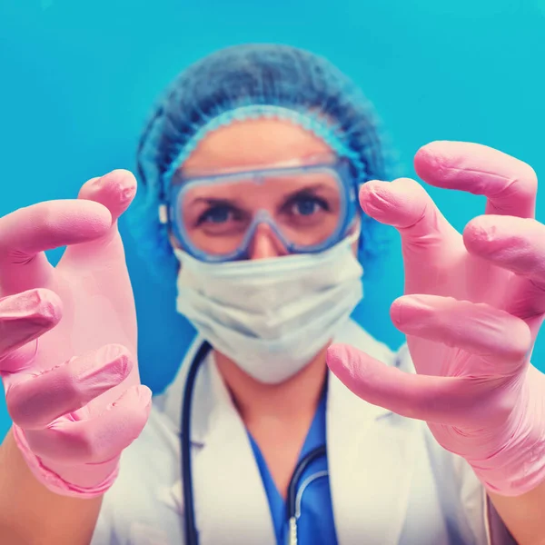 Hands of a doctor with an angry look are drawn to the patient as in a horror movie, blue background. Concept stay home. A nurse reaches for you in medical gloves, a nightmare close-up.