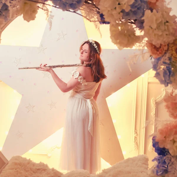 A female musician plays the flute in a white dress. Flautist with a musical instrument on the background of a star, studio portrait