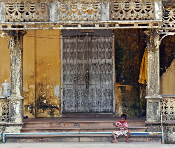 小さなビルマの少年座って 老朽化した 古い黄色の建物の手順で遊んで マワラミンミャンマー 高品質の写真 — ストック写真