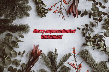 Merry unprecedented Christmas, positive message in bright red letters in a circle of holly and pine leaves for 2020 with pandemic. High quality photo clipart