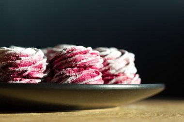 Ahşap masadaki siyah tabakta duran pembe şekerleme ve sert bir güneş ışığı. Makro zephyr.