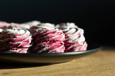 Ahşap masadaki siyah tabakta duran pembe şekerleme ve sert bir güneş ışığı. Makro zephyr.