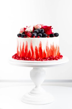 Düğün pastası beyaz ve kırmızı renklerle süslenmiş güller ve üzerine toz şeker serpiştirilmiş üzümler. Beyaz arka plandaki beyaz stantta pasta.