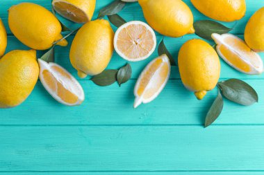 Turkuaz ahşap arka planda yaprakları olan taze kesilmiş limonlar. Alt kopya alanı ile yukarıdan görüntüle.