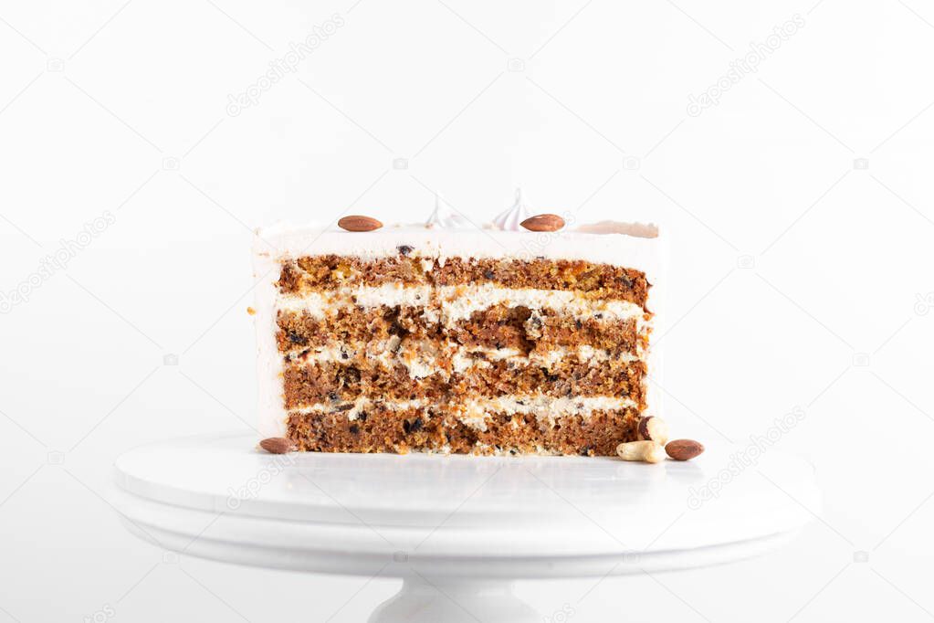 Carrot cake slice with almond nuts on the white stand. Cake cut on white background.