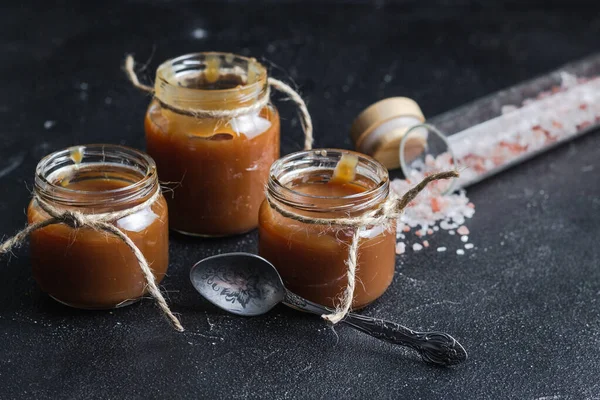 Homemade salted caramel sauce in jars and caramel candies with a vintage spoon on the black background. Macro shot