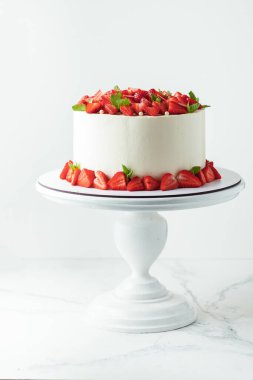 Beyaz pasta standında çilek ve nane yapraklarıyla süslenmiş beyaz tereyağlı pasta.