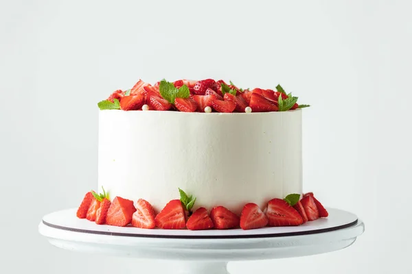 White buttercream cake decorated with strawberries and mint leaves on the white cake stand