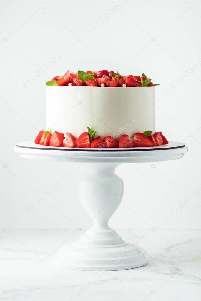 White buttercream cake decorated with strawberries and mint leaves on the white cake stand