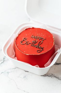 Kırmızı doğum günü pastası. Üstünde komik bir tebrik mesajı olan beyaz bir hediye kutusunda..