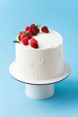 Taze ahududu ve böğürtlenlerle süslenmiş beyaz krem peynirli doğum günü pastası. Mavi arka planda kırmızı ve siyah böğürtlenli zarif yaz pastası