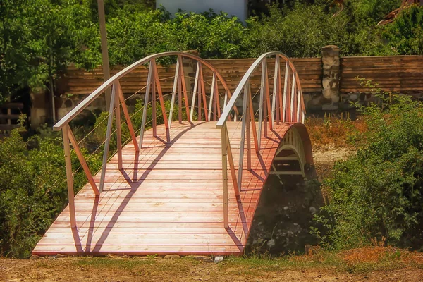 Güneşli bir günde vadiden geçen metal parmaklıklı çelik bir çerçevede tahta köprü.
