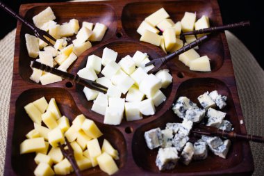 Gouda peynirli ahşap peynir tahtası, taze parmesan, parmesan ve gorgonzola, üstünde siyah bir masa.