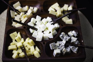 Gouda peynirli ahşap peynir tahtası, taze parmesan, parmesan ve gorgonzola, üstünde siyah bir masa.