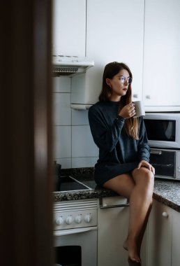 Genç bir kadın sabah kahvesini evinde içiyor. 