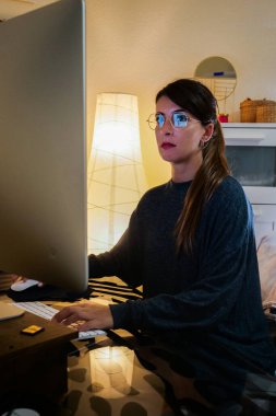 Genç bir kadın odasında bilgisayarla telgraf çekiyor.