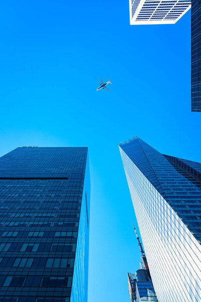 Low angle view of modern office buildings and aircraft against sky in Midtown of Manhattan