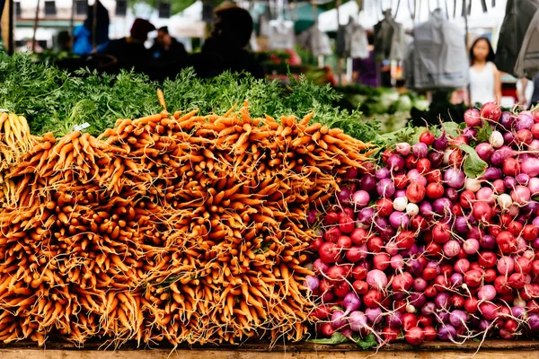 Orange baby carrots and radish piled in market — Stock Photo, Image