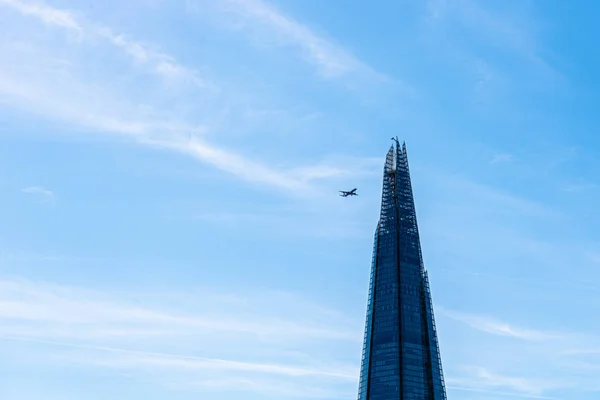 Mavi gökyüzüne karşı gökdelenin üzerinde uçan uçak — Stok fotoğraf