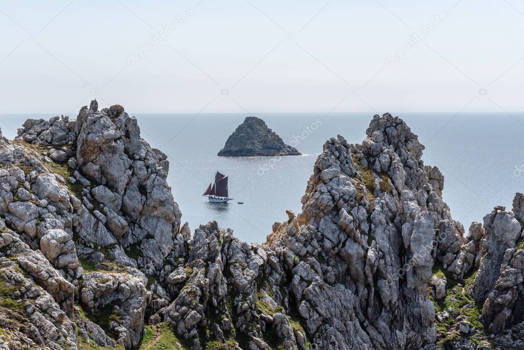 sailboat sailing in the sea among rocks
