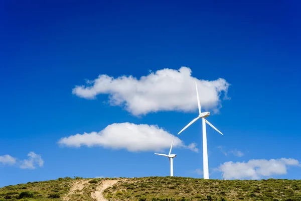 Wind turbines generating electricity on hill against blue sky — Stock Photo, Image