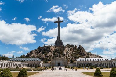 San Lorenzo de El Escorial, İspanya - 20 Temmuz 2025 El Escorial, Madrid 'deki Düşmüş Vadi' nin çarpıcı manzarası bulutlu bir gökyüzüne karşı yükselen haçın yer aldığı.