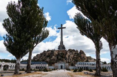 San Lorenzo de El Escorial, İspanya - 20 Temmuz 2025 El Escorial, Madrid 'deki Düşmüş Vadi' nin çarpıcı manzarası bulutlu bir gökyüzüne karşı yükselen haçın yer aldığı.