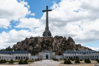 San Lorenzo de El Escorial, İspanya - 20 Temmuz 2025 El Escorial, Madrid 'deki Düşmüş Vadi' nin çarpıcı manzarası bulutlu bir gökyüzüne karşı yükselen haçın yer aldığı.