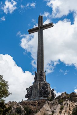 San Lorenzo de El Escorial, İspanya - 20 Temmuz 2025 El Escorial, Madrid 'deki Düşmüş Vadi' nin çarpıcı manzarası bulutlu bir gökyüzüne karşı yükselen haçın yer aldığı.