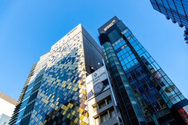 Tokyo, Japonya - 3 Ağustos 2024: Ginza, Tokyo 'da modern mimari, açık mavi gökyüzü altında cam cepheli yüksek binalar.