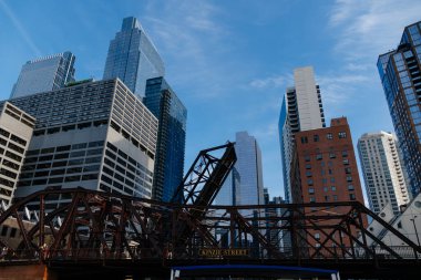 Alçak açılı bir çekim, parlak mavi gökyüzü altında paslı bir asma köprü ve sayısız gökdelenle Chicago 'nun gökyüzünü yakalıyor..