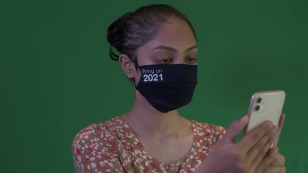 2021年にフェイスマスクを着用した若いアジアの女性がスマートフォンを保持しています 緑の画面 ロックオフ — ストック動画