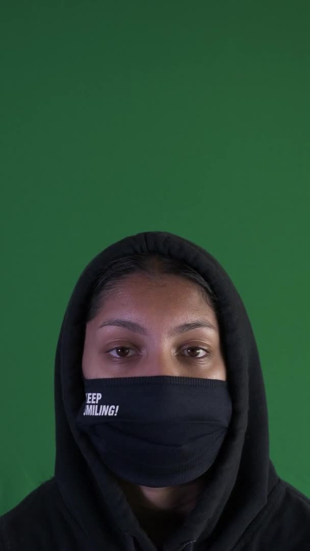 女性のティーンエイジャーを身に着けているパーカーと笑顔の顔マスクを保ちます 垂直ビデオ 緑の画面 ロックオフ — ストック動画