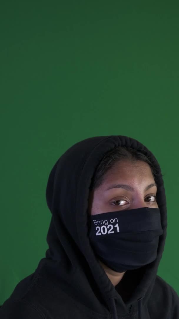 女性のティーンエイジャーを身に着けているパーカーとそれを持って来ます2021フェイスマスク 垂直ビデオ 緑の画面 ロックオフ — ストック動画