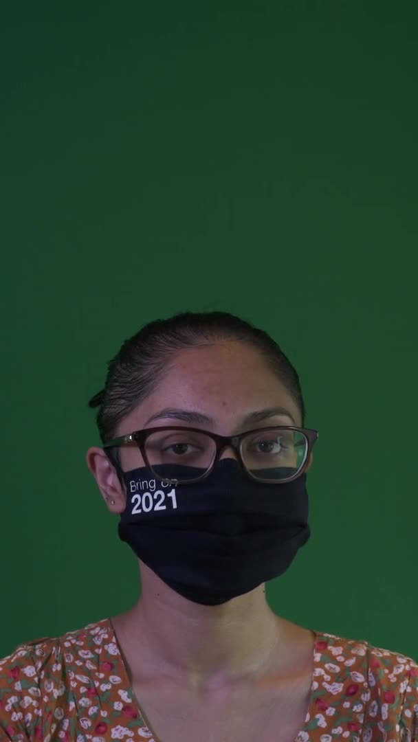 2021年に顔マスクと眼鏡をかけてカメラを見る若いアジア人女性 垂直ビデオ 緑の画面 — ストック動画