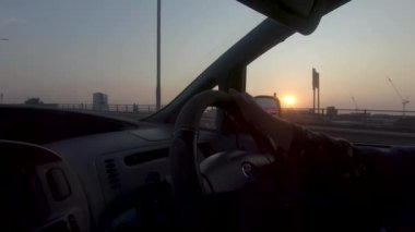 Gün batımında otopark yolunda direksiyonda kadın ellerini yakın tut. Görüntüyü Takip Et