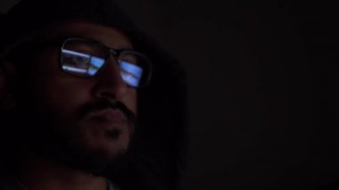 Kapüşonlu Asyalı erkek, karanlık odada gözlüklü bilgisayar ekranlarının yansıması. Kilitli