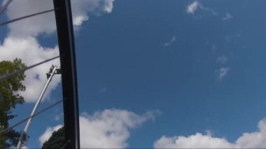 POV, bisikletle ağaçların önünden geçerken bulut bulutlarıyla Mavi Gökyüzüne bakıyor. Görüntüyü Takip Et