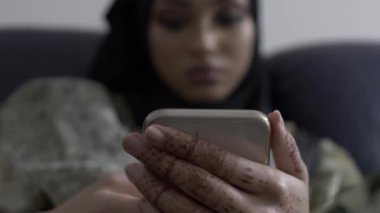 İçerde oturan, akıllı telefonuna bakan Müslüman bir kadın. Sığ Odaklanma, Düşük Açı, Kapalı