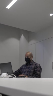 Dizüstü bilgisayarda maske takan, sıradan, zeki bir yetişkin erkek. Dikey Video, Kapalı, Düşük Açı