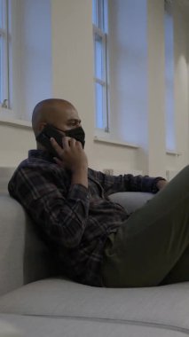 Ofis koltuğunda oturan, yüz maskesi takan, cep telefonu kullanan akıllı, sıradan bir erkek. Dikey Video, Kilitli
