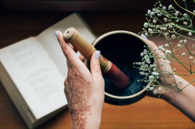 Kına dövme bir çiçek arka plan üzerine açık kitap üzerine Tibet şarkı kase tutan eller kaplı. Meditasyon ve ilham ruh hali