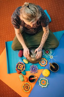 Mat sınıf iplik, önünde oturan parmak ile asmak davul çalmaya elinde kına dövme genç sarışın beyaz adamla mandalalar ördü. Üstten görünüm.