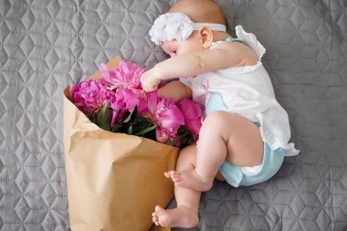 Yatakta yatıyordu ve ping buket pion çiçek ile oynarken mutlu yeni doğan bebek