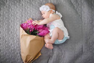 Yatakta yatıyordu ve ping buket pion çiçek ile oynarken mutlu yeni doğan bebek
