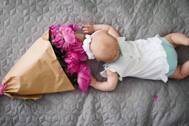 Yatakta yatıyordu ve ping buket pion çiçek ile oynamaya yeni doğan bebek